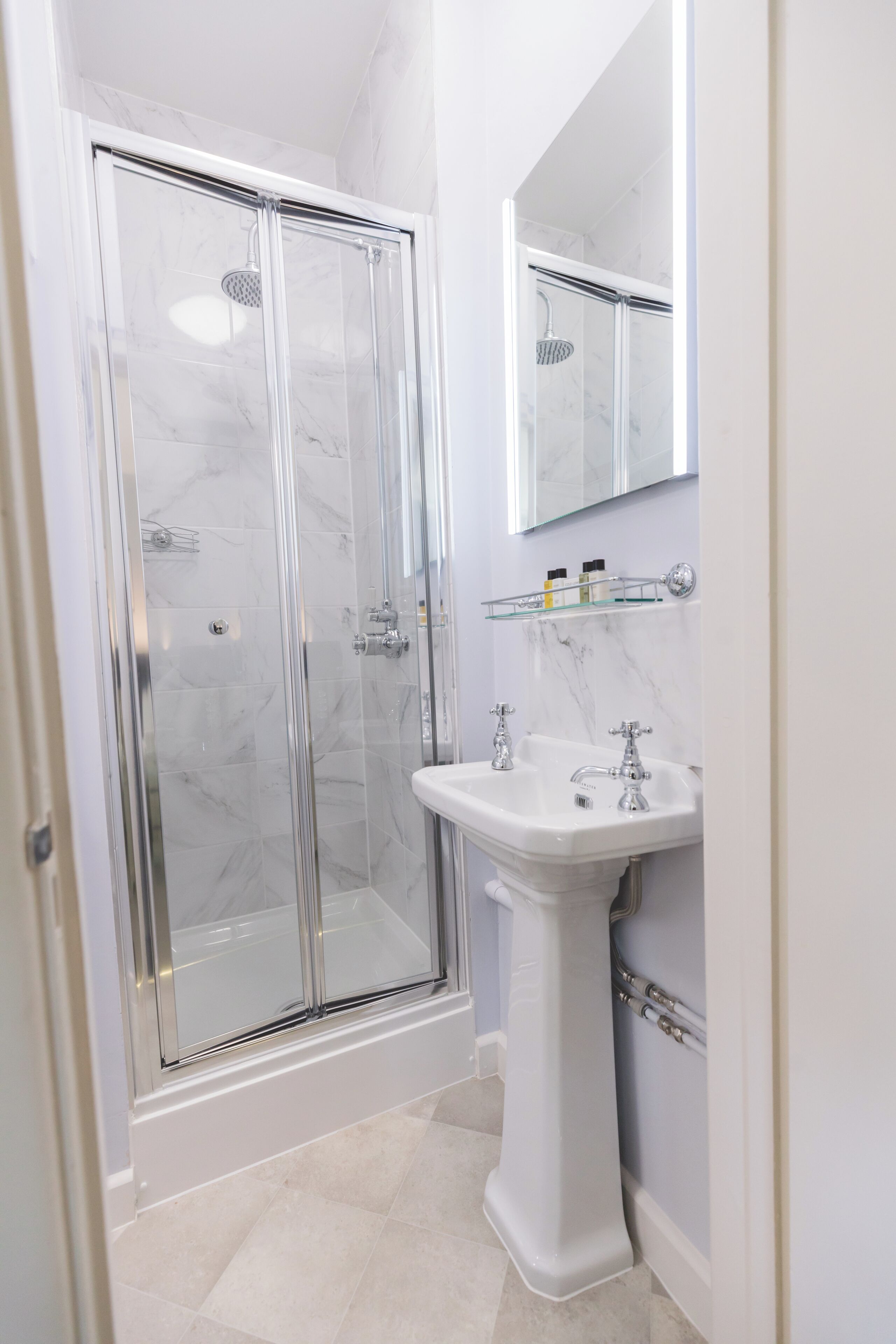 A modern bathroom with a glass shower enclosure, a pedestal sink, and a marble backsplash.
