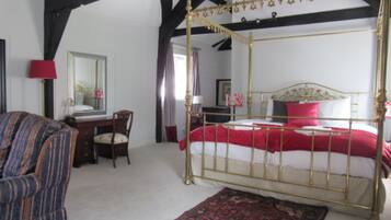 Een hemelbed met een rode en witte spreideken, een houten stoel, een bureau met een lamp en een spiegel aan de muur.