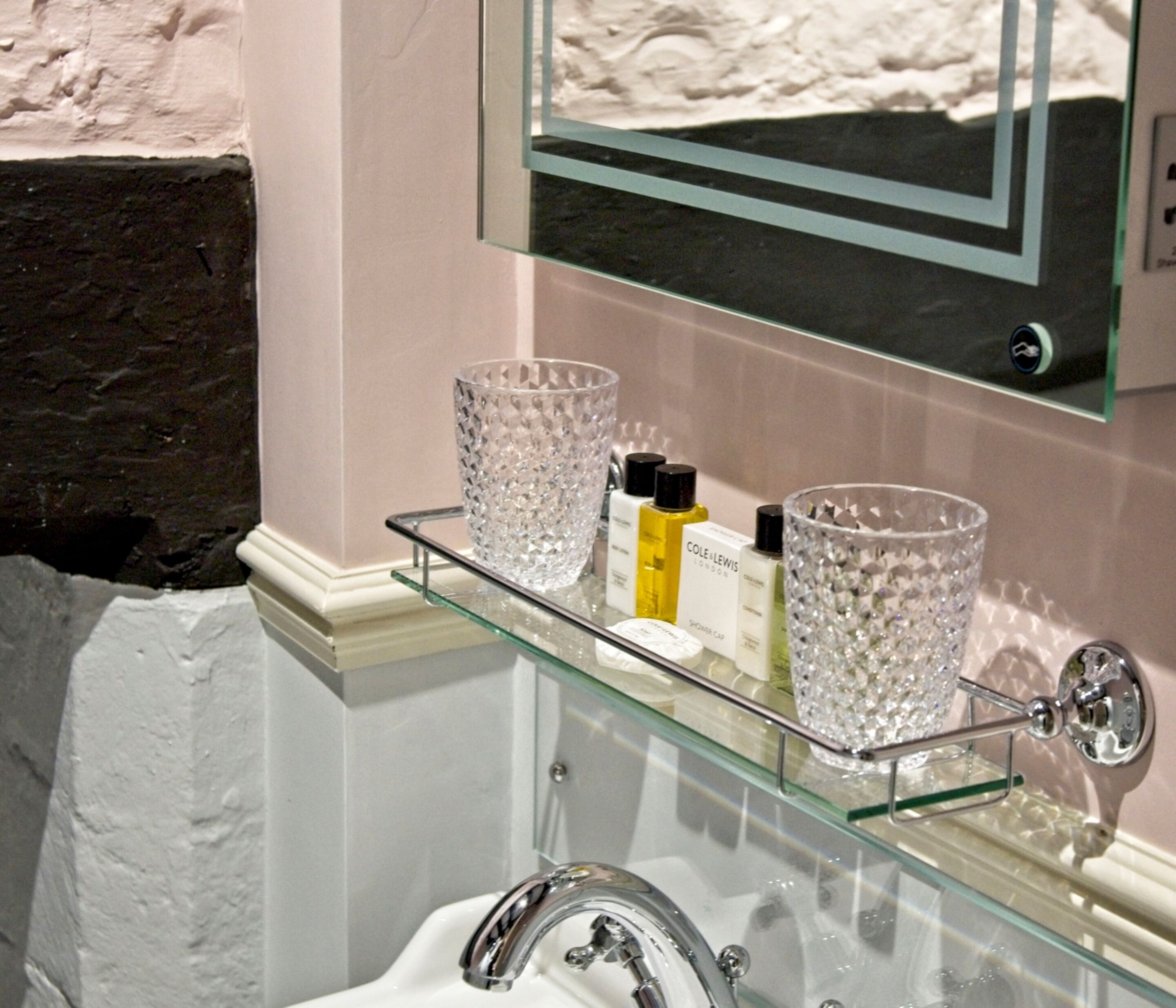 A bathroom with a glass shelf holding toiletries and two crystal glasses.