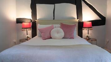 Un dormitorio con una cama blanca, almohadas rosadas y blancas, dos lámparas de noche y una viga de techo de madera oscura.