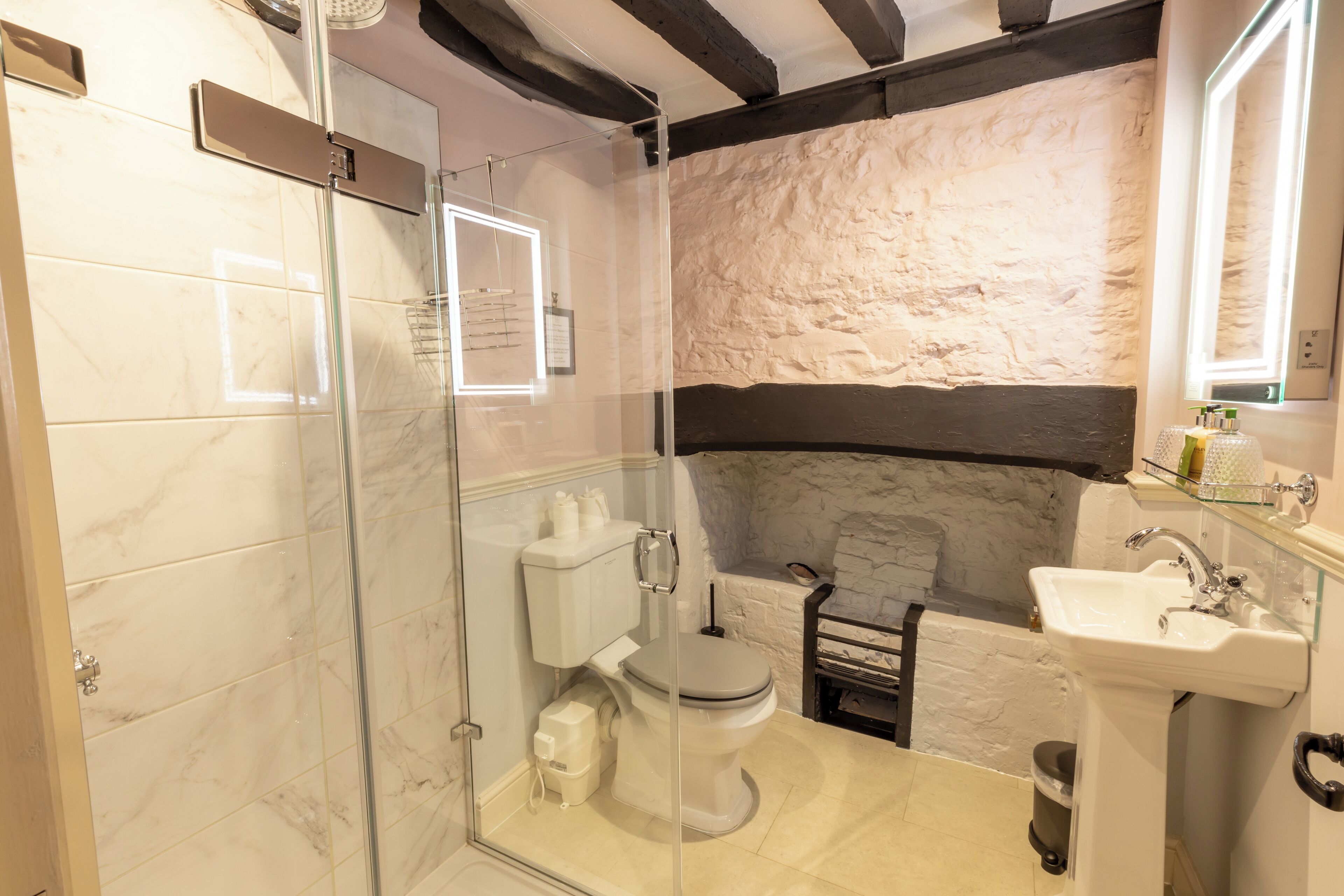 Une salle de bain avec une douche à parois de verre, des toilettes, un lavabo et un mur en pierre en arrière-plan.