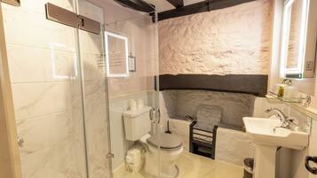 Une salle de bain avec une douche à parois de verre, des toilettes, un lavabo et un mur en pierre en arrière-plan.
