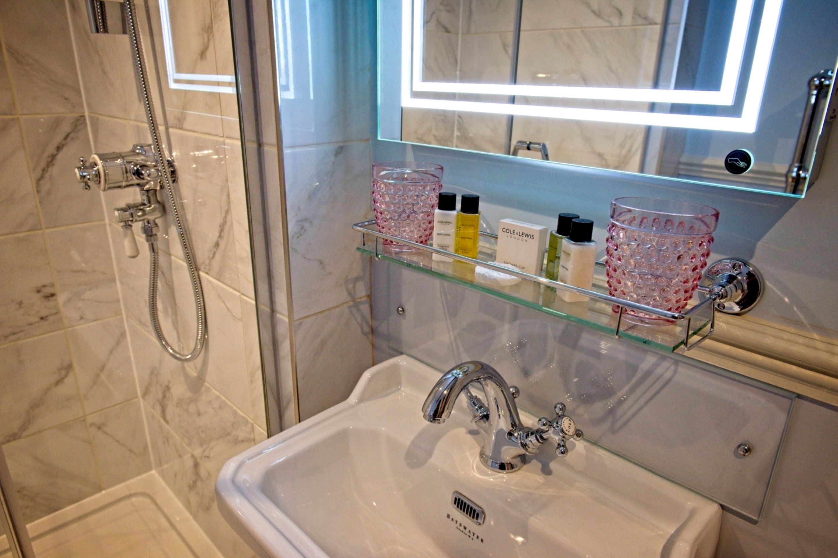 Een badkamer met een glazen plankje met toiletartikelen, een wastafel met een moderne kraan en een douche met een handdouche.