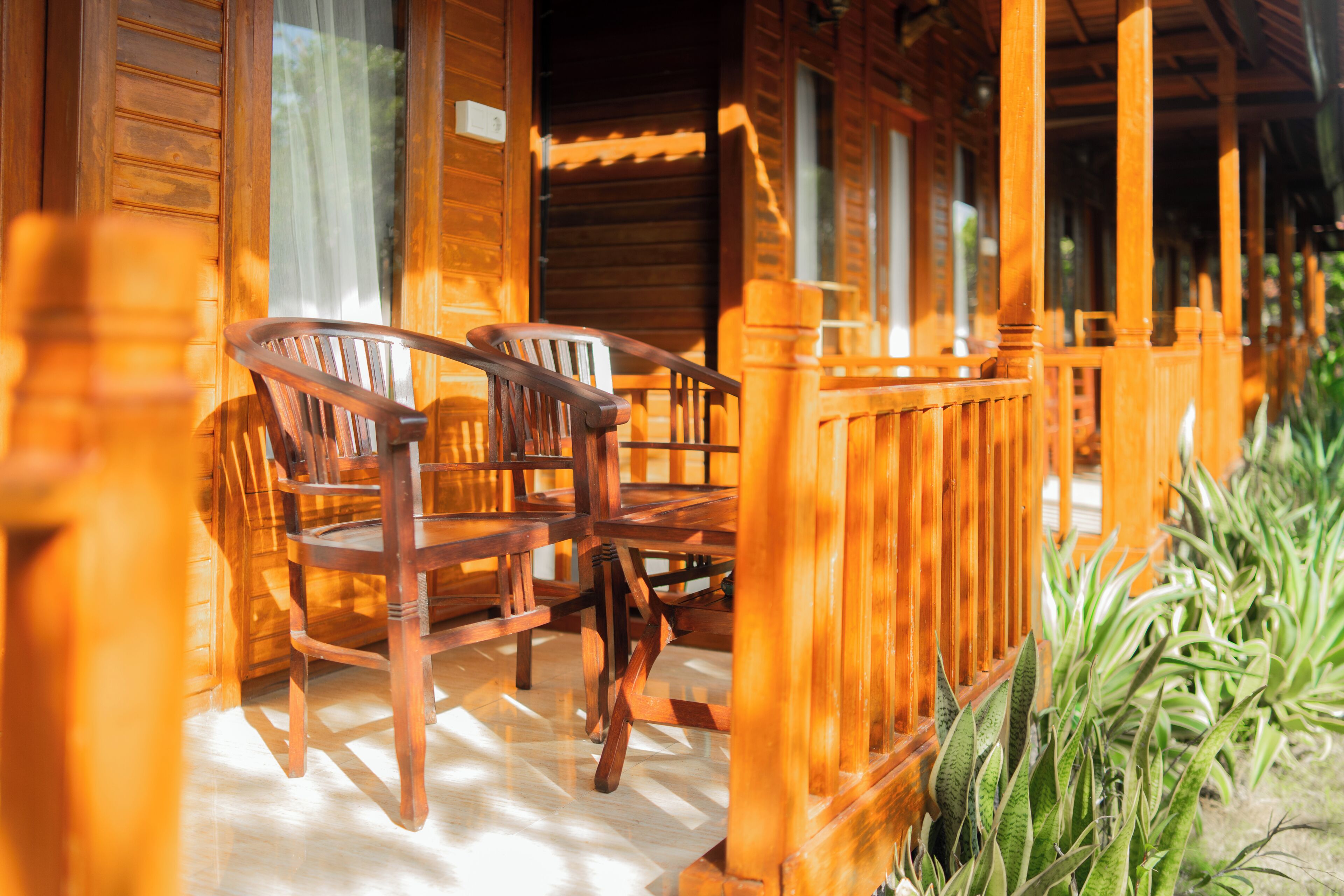 A wooden cabin with a porch, wooden chairs, and a wooden fence.