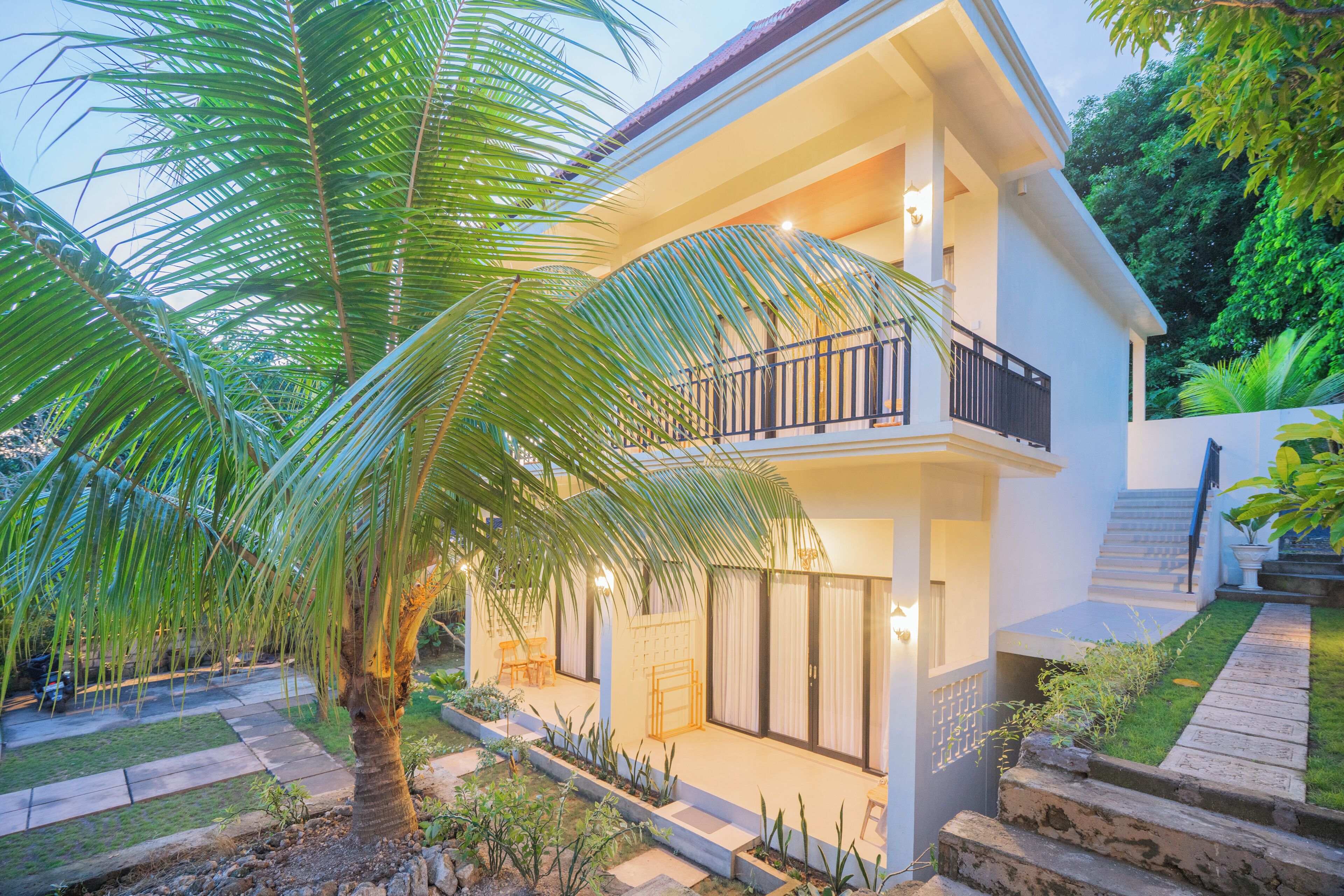 A two-story house with a balcony, a palm tree, and a well-maintained garden.