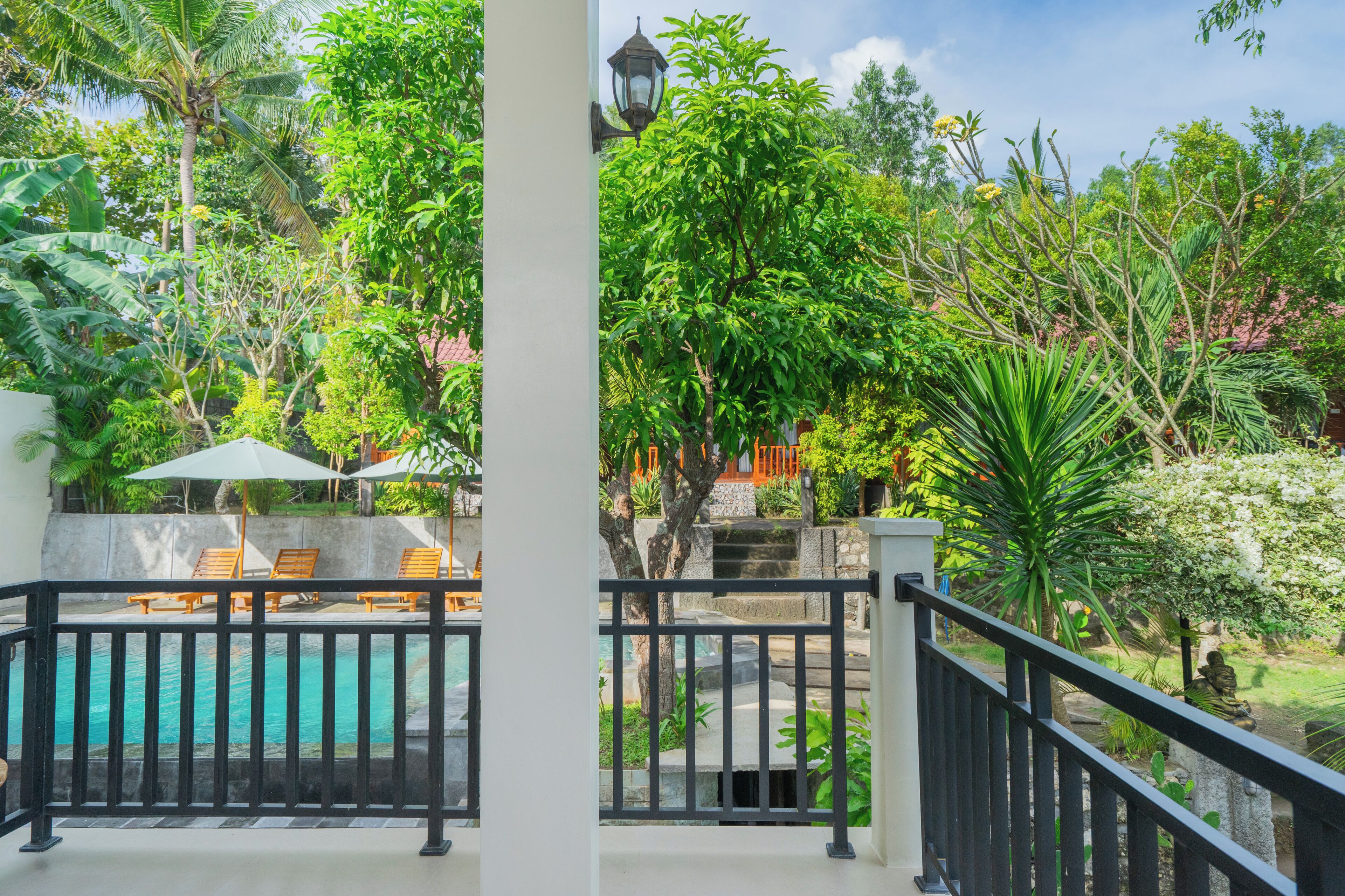 A poolside area with a view of lush greenery, a white building, and a black railing.