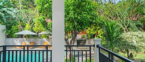 A poolside area with a view of lush greenery, a white building, and a black railing.