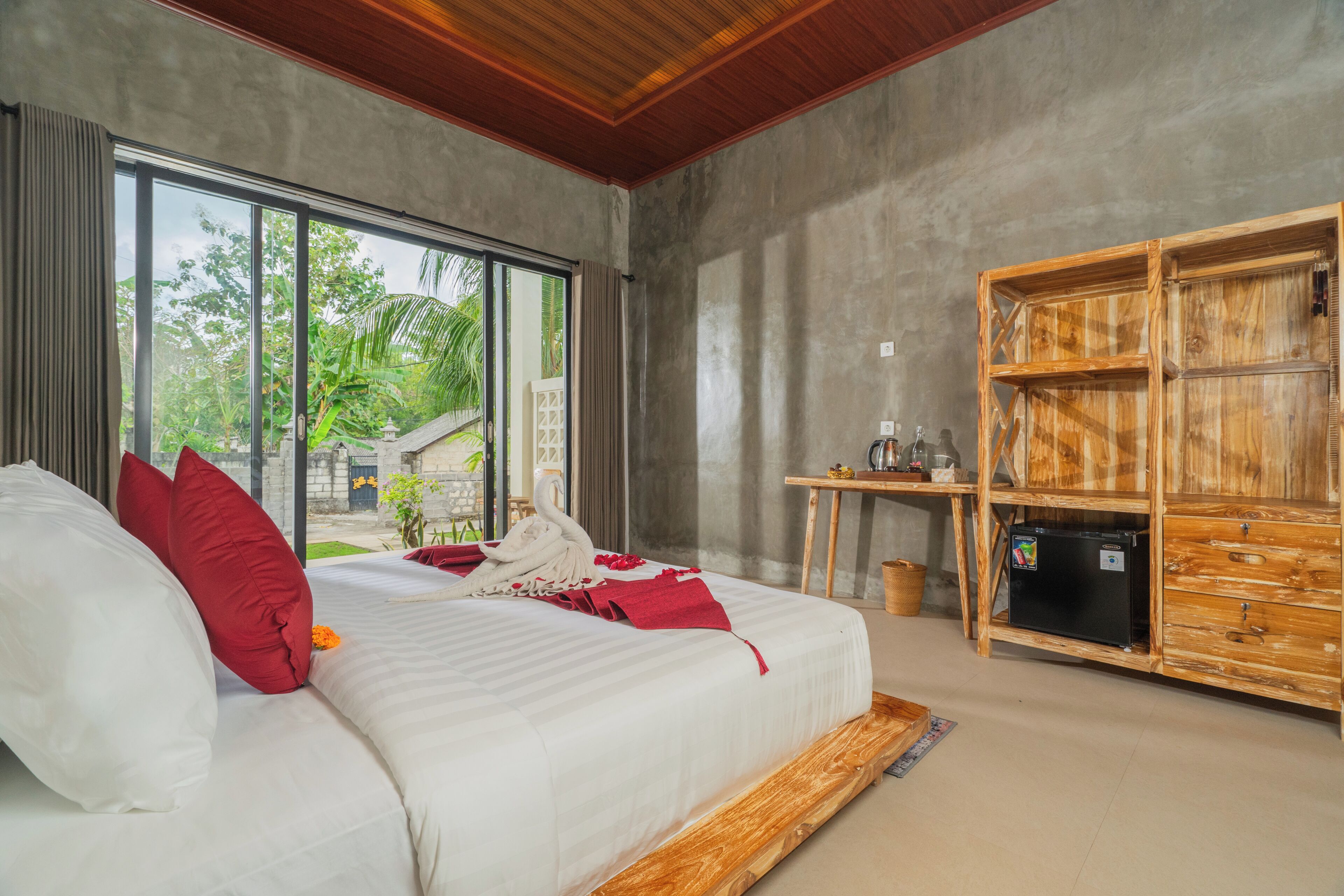 A bedroom with a large bed, a wooden cabinet, and a view of greenery outside.