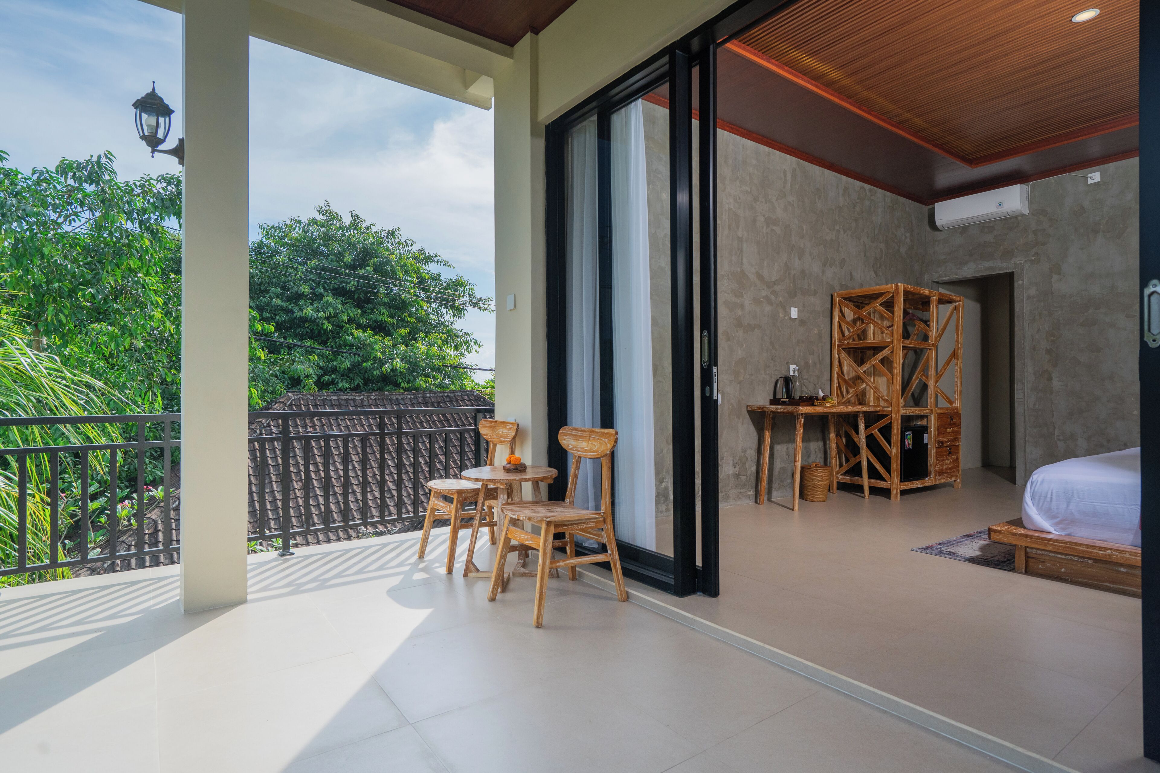 A balcony with a table and chairs, a bed, and a wooden structure in a room with large windows.