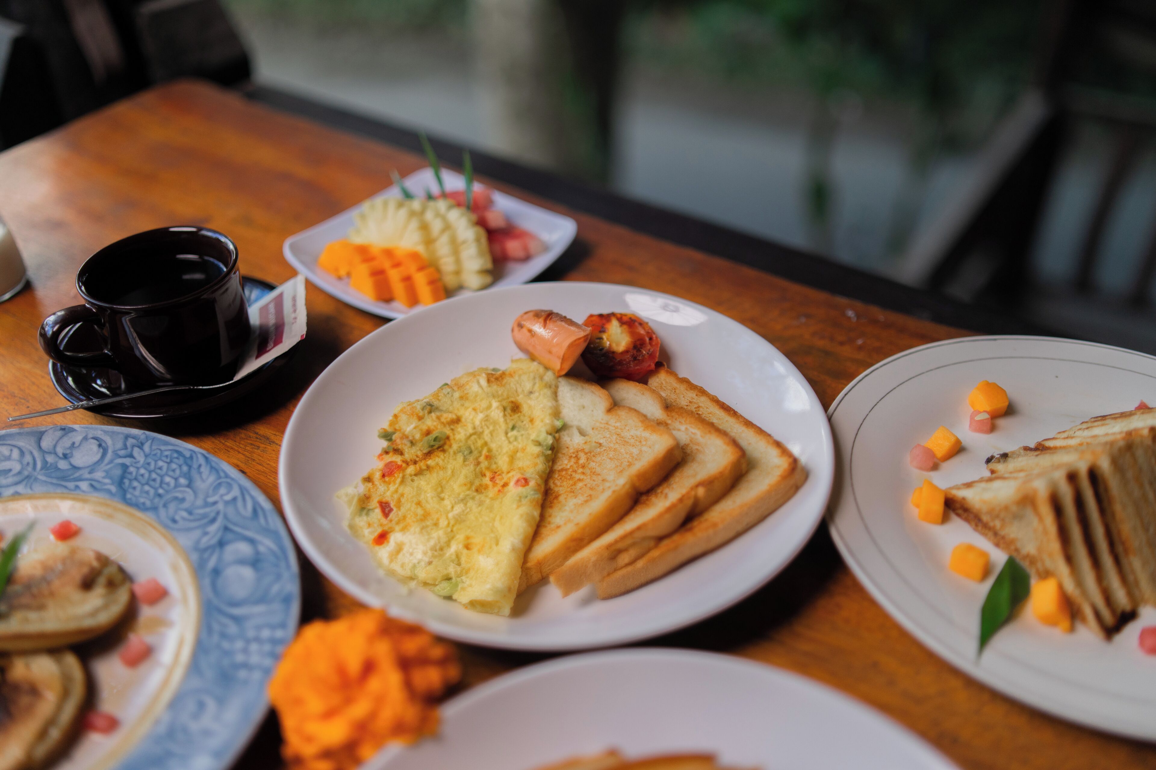A dining table with various dishes including toast, a plate of sliced fruit, and a cup.