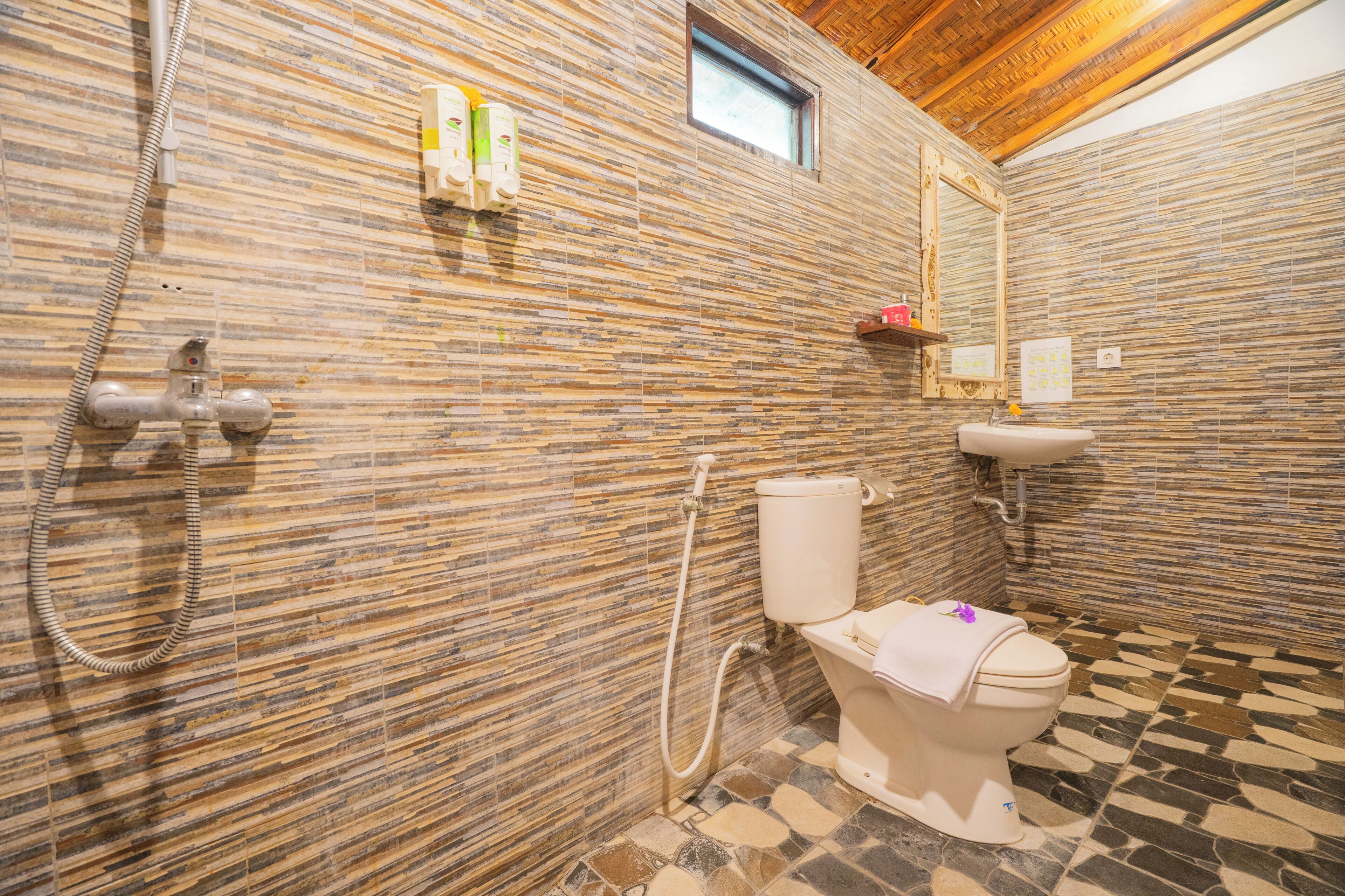 A bathroom with a stone-patterned wall, a toilet, a shower, and a small window.