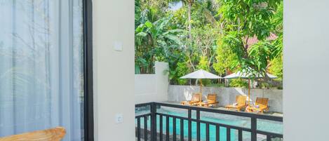 A balcony with a pool, wooden chairs, and umbrellas.