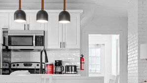 Une cuisine moderne avec des meubles blancs, une table à manger avec des chaises et des luminaires suspendus.