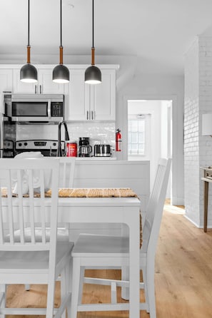 A modern kitchen with white cabinetry, a dining table with chairs, and pendant lights.
