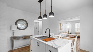 Une cuisine moderne dotée d’un îlot central, de meubles blancs, d’une cuisinière intégrée et de luminaires suspendus.