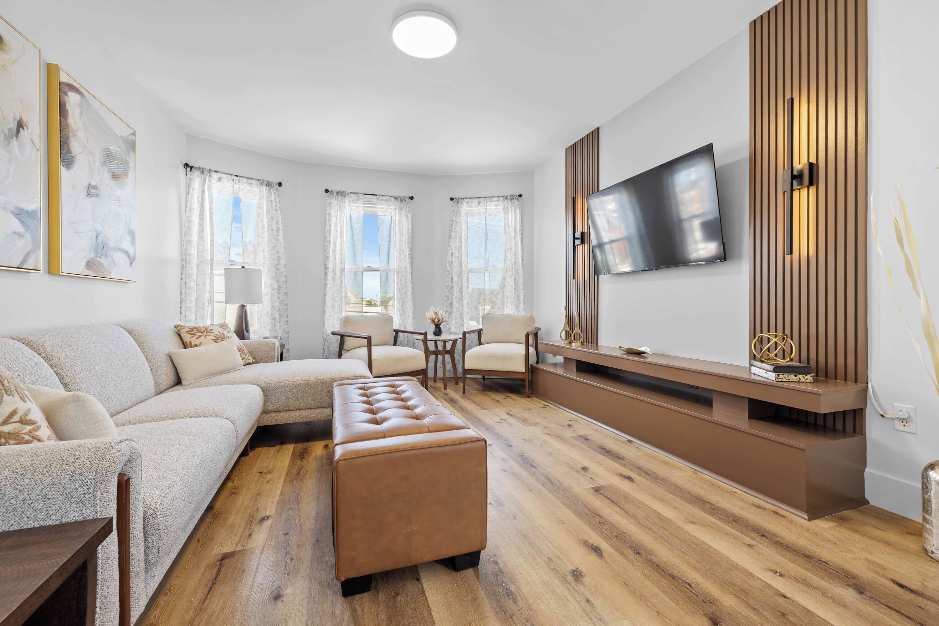 A modern living room with a sofa, ottoman, and a TV mounted on the wall.