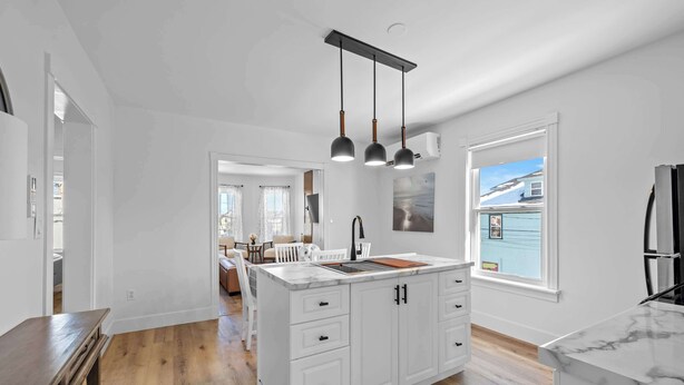Une cuisine spacieuse avec des meubles blancs, un plan de travail en marbre et des luminaires suspendus.