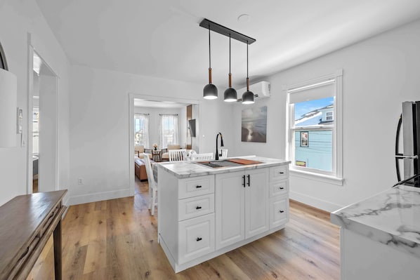 A spacious kitchen with white cabinetry, a marble countertop, and pendant lighting.