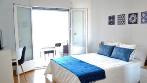 Un dormitorio con cama, escritorio, silla y balcón.