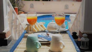 Desayuno con dos vasos de zumo de naranja, una tetera, una jarra y un plato con cubiertos junto a una piscina.