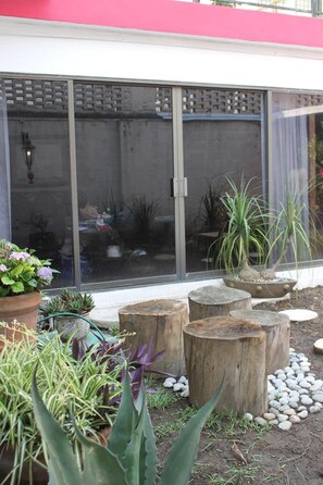 A garden area with potted plants, wooden stumps, and a glass door leading to a room.
