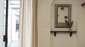 Vista del interior con una puerta que da a un espacio exterior, un espejo en la pared y un estante pequeño con un florero.