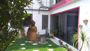 Un patio con una escultura, plantas en macetas y un edificio de techo rojo y amplias ventanas.