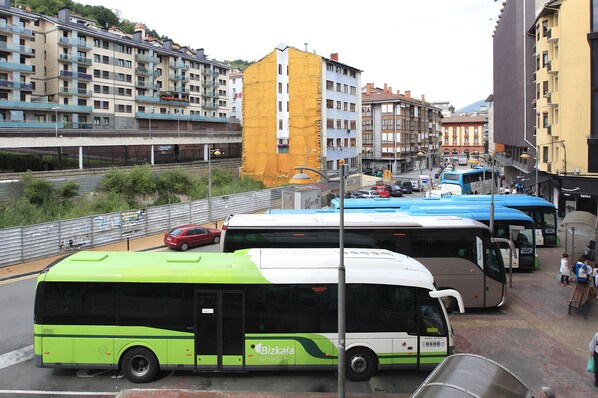 Una calle urbana con varios autobuses estacionados al borde de la calzada, un paso de peatones y edificios al fondo.