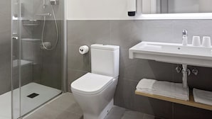 A modern bathroom with a glass shower enclosure, a white toilet, a sink with a mirror above, and a towel rack. - Eibarrooms (Eibar)