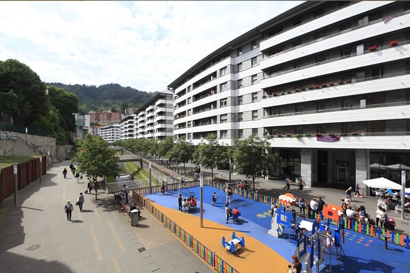 A multi-story hotel with balconies, a playground area, and a pedestrian walkway.
