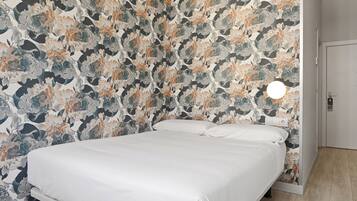 A bedroom with a floral wallpaper, a white bed, and a round light fixture on the wall.