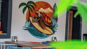 Interior de restaurante con un mural de una tortuga surfando, mesas, sillas y una barra de madera.