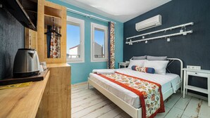 A bedroom with a bed, a bedside table, a hanging light, a window, and an air conditioning unit. - İsinda Pansiyon (Kas)