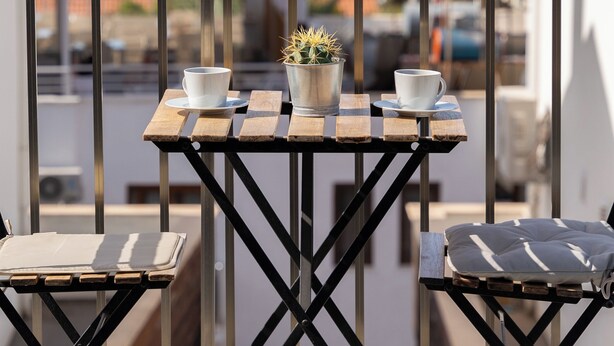 A balcony with a table and chairs, a potted plant, and a view of the sea and mountains. - İsinda Pansiyon (Kas)