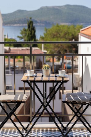 A balcony with a table and chairs, a potted plant, and a view of the sea and mountains. - İsinda Pansiyon (Kas)