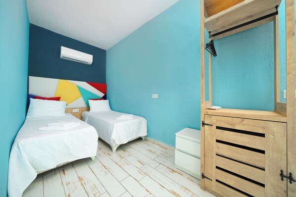 A room with two beds, a wooden cabinet, and a colorful abstract wall art. - İsinda Pansiyon (Kas)