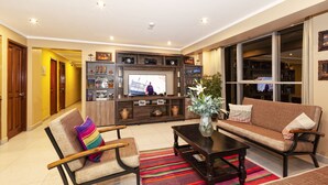 A living room with a sofa, armchair, coffee table, TV, and shelves with decorative items.