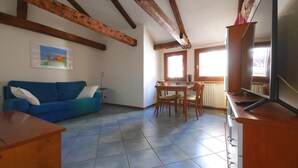 Un salon avec un canapé bleu, une table à manger en bois et des chaises. On y trouve un téléviseur posé sur un meuble en bois et un tableau accroché au mur.