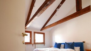 Une chambre à coucher avec un lit, des poutres en bois, une fenêtre et un radiateur.