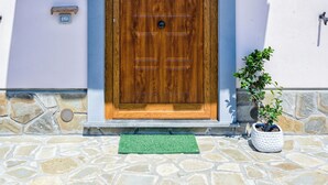 A wooden door with a green mat, a potted plant, and two wall-mounted lights.