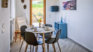 A dining area with a round table, chairs, a vase with flowers, a lamp, and a bookshelf.