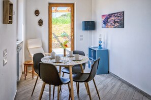 A dining area with a round table, chairs, a vase with flowers, a lamp, and a bookshelf.