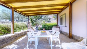 An outdoor patio with a wooden pergola, stone flooring, a white table with chairs, and a view of the surrounding landscape.