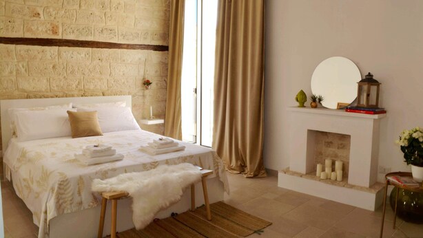 A bedroom with a large bed, a wooden bench, a fireplace, and a view of the outdoors. - Apricot House. In the heart of the old town. (Bari)