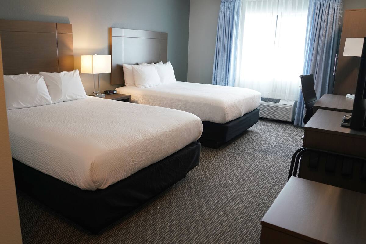 A hotel room with two beds, a desk, a chair, a TV, and a window with curtains.