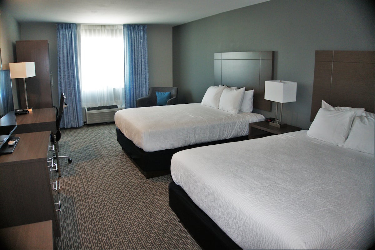 A hotel room with two beds, a desk, a chair, a lamp, and a window with curtains.