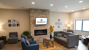 A modern lounge area with a stone fireplace, comfortable seating, and a large window providing natural light. - Brookstone Fort Dodge (Fort Dodge)
