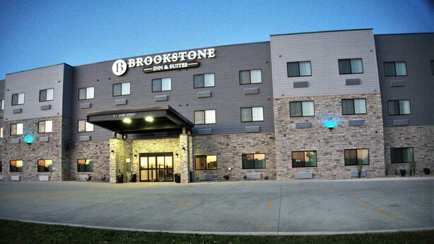 A multi-story hotel with a stone facade, a prominent sign reading "BROOKSTONE INN & SUITES," and a parking lot in front. - Brookstone Fort Dodge (Fort Dodge)