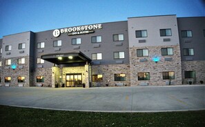 A multi-story hotel with a stone facade, a prominent sign reading "BROOKSTONE INN & SUITES," and a parking lot in front. - Brookstone Fort Dodge (Fort Dodge)