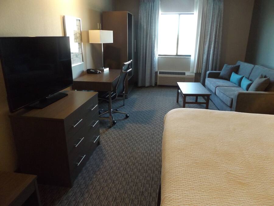 A hotel room with a bed, a desk with a chair, a television, a lamp, and a sofa.